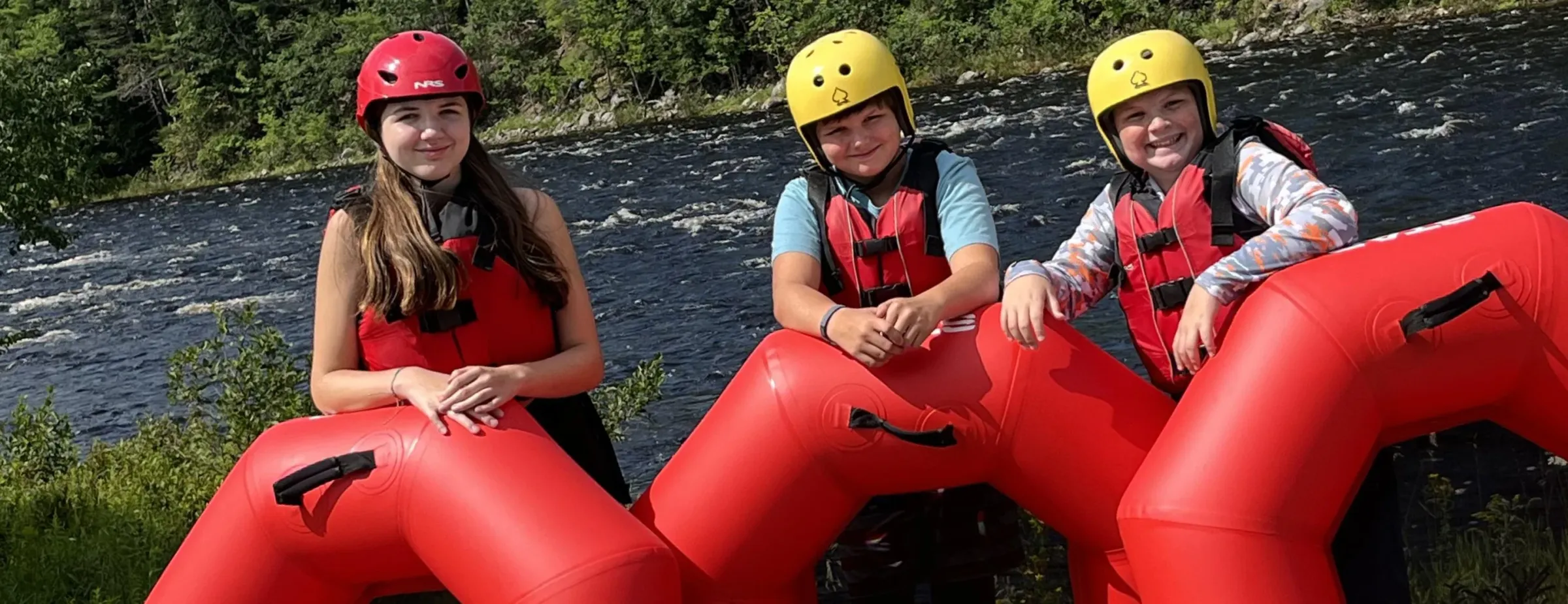 Three guests with red river tubes and safety gear beside the Hudson River